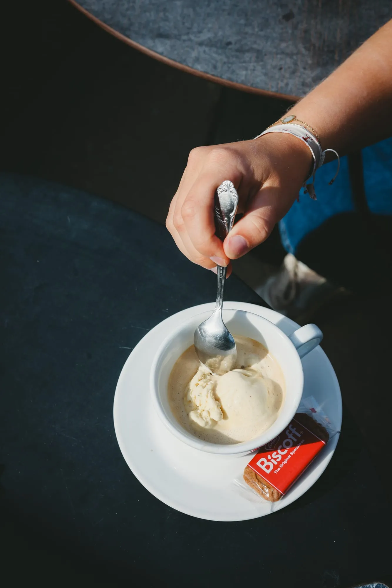 Une main plonge une cuillère dans une tasse de café et de glace, un biscuit Biscoff sur la soucoupe.