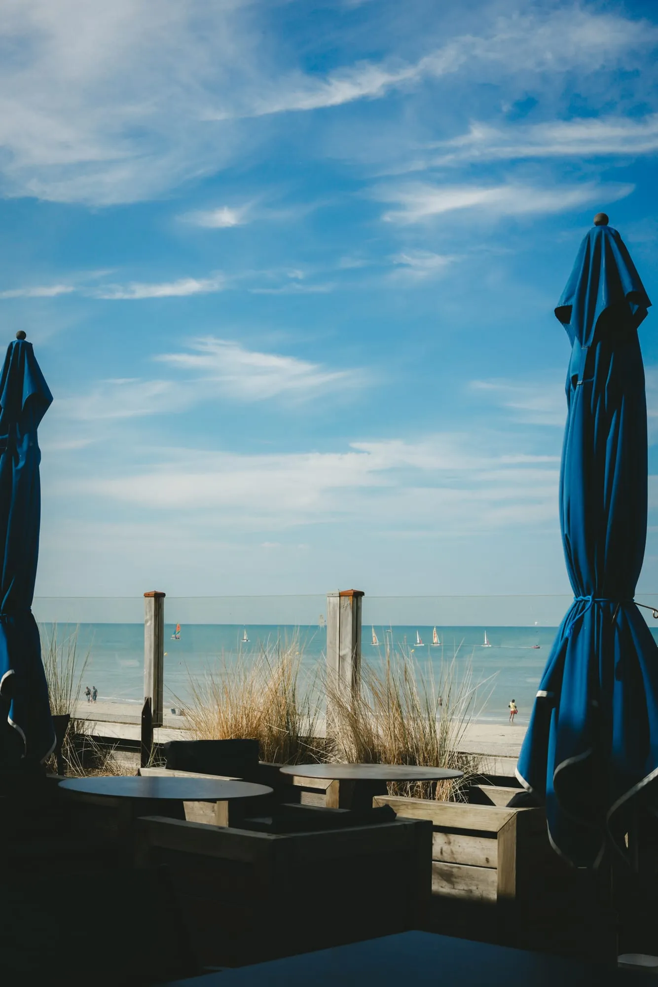 La terrasse de L’Océan : parasols bleus repliés, tables face à la plage et à la mer.